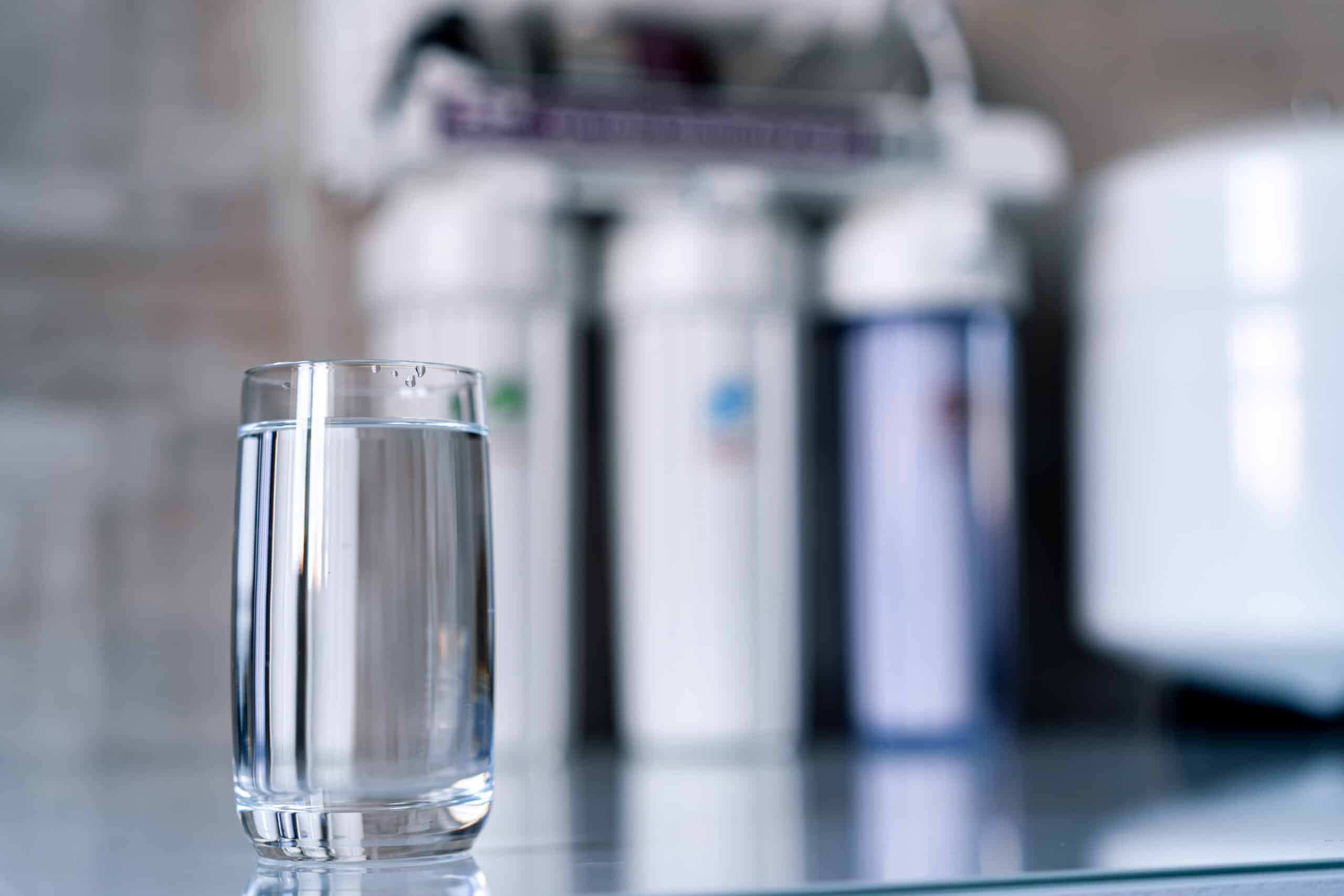 Pure water in glass and water filters on the blurred background. Household filtration system.